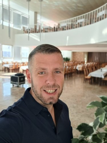 Svadobný moderátor Martin Matuška v modrom obleku s mikrofónom v ruke počas príhovoru na svadobnej hostine.