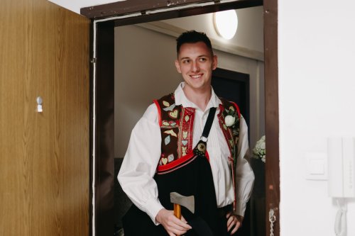 Bíž Starejší v tradičnom slovenskom ľudovom kroji s valaškou v rukách počas svadobnej odobierky pri dverách.