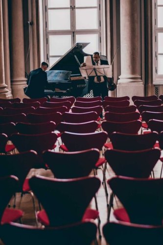 Hudobníci pripravujúci sa na vystúpenie Bridgerton Violin Experience s klavírom a husľami v elegantnej koncertnej sále.