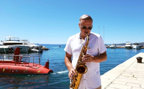 Jozef Ježík z Duo Royal hrá na saxofón v prístave pri mori počas slnečného dňa.