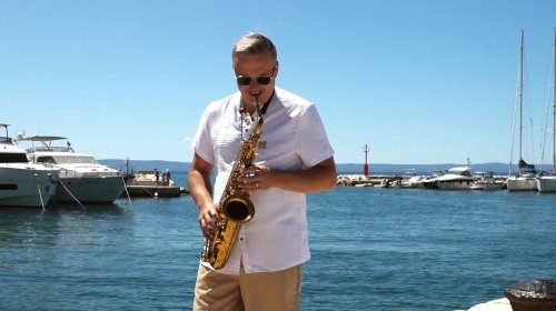 Jozef Ježík z Duo Royal hrá na saxofón v prístave pri mori počas slnečného dňa.