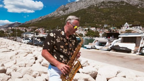 Jozef Ježík z Duo Royal hrá na saxofón v prístave pri mori počas slnečného dňa.