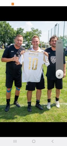 Traja muži na futbalovom ihrisku počas kultúrnej akcie držia biely dres s číslom desať a menom Kuchta.