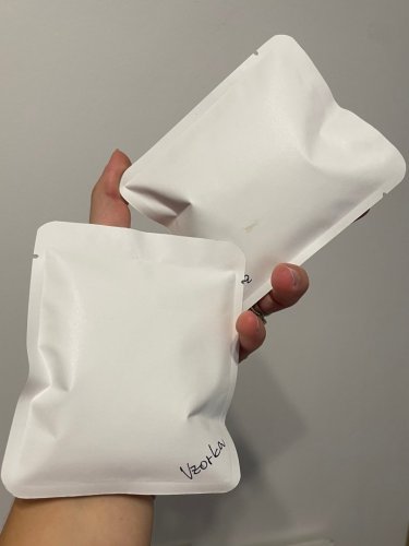 Ruka drží dve biele mini kávové balíčky ako vzorky svadobných darčekov pre hostí.