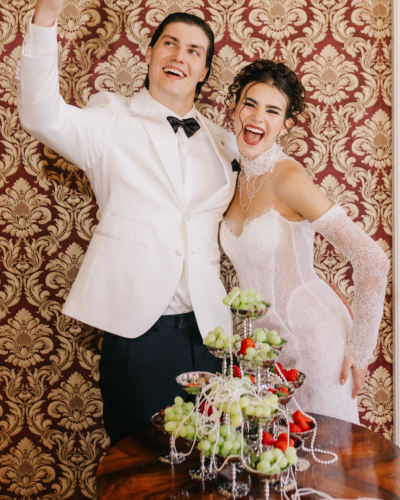 Rozradostnený svadobný pár pózuje pri luxusnom ovocnom bare s hroznom a jahodami v rámci eventu od Monarché - curated wedding and events.