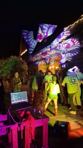 Hostia sa zabávajú na nočnej svadobnej párty s pestrofarebným svetelným projektorom a DJ technikou v popredí.