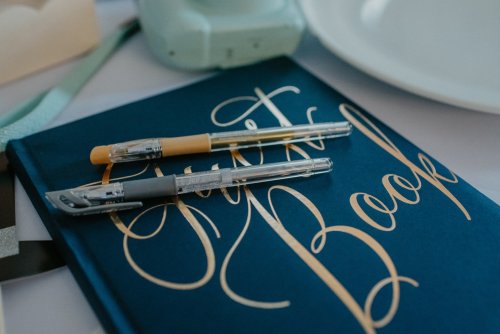 Elegantná tmavomodrá kniha hostí so zlatým písmom a perami, pripravená svadobnou koordinátorkou Saskiou - Wedding Fairy.