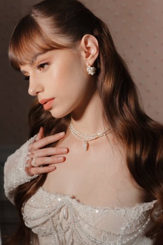 Elegantná nevesta v čipkovaných svadobných šatách zdobených perlami s jemným perlovým náhrdelníkom a náušnicami.