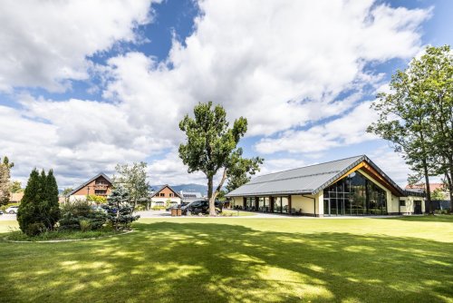 Exteriér moderného objektu Humno Demänová - event house so skleneným priečelím a upraveným trávnikom počas slnečného dňa.