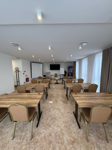 Moderne zariadená kongresová miestnosť v Restaurant Azuro so školským sedením, drevenými stolmi a prezentačnou technikou.