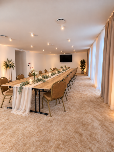 Elegantne vyzdobený dlhý stôl v kongresovej miestnosti Restaurant Azuro pripravený na oslavu s bielymi kvetmi a sviečkami.