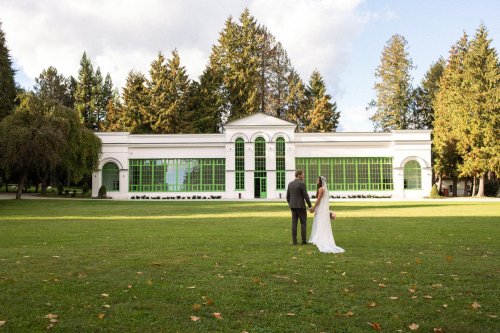 Novomanželský pár stojaci v parku pred elegantnou bielou historickou budovou Kaštieľa Chateau Révay s výraznými zelenými oknami.