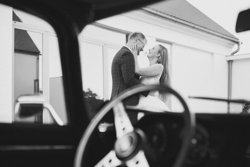 Čiernobiela fotografia smejúceho sa novomanželského páru v areáli Machovský Dvůr, zachytená cez okno auta.