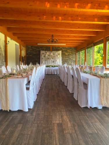 Svadobná hostina v Reštaurácii Pod lipami s elegantne prestretými dlhými stolmi v presvetlenej miestnosti s dreveným stropom.