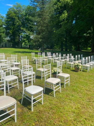 Elegantné biele chiavari stoličky pripravené na svadobný obrad v exteriéri reštaurácie Pod lipami obklopenej zeleňou.