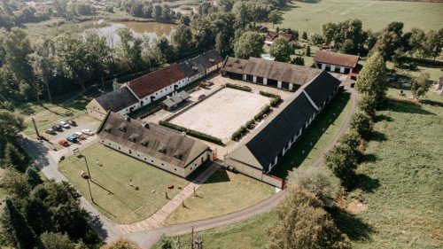 Letecký pohľad na historický vidiecky areál s bielymi budovami a nádvorím uprostred zelenej prírody